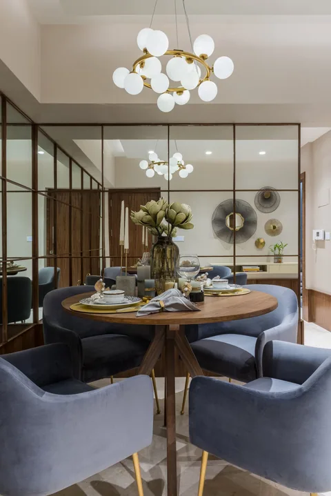 A round four-seat dining table fitted into the living-room corner of a Mumbai two-bedroom show apartment