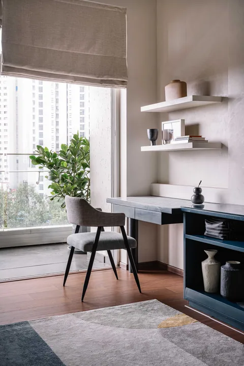 A fitted study corner in a Mumbai apartment with a desk, chair, open shelves and a window seat