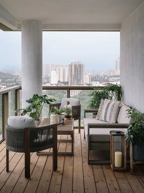 A Mumbai apartment balcony with woven chairs, a small table, plants and a view across the city