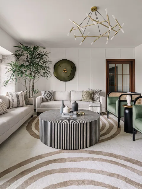 An Indian apartment living room in Mumbai with a neutral sectional sofa, a green chair, brass lighting and a patterned rug