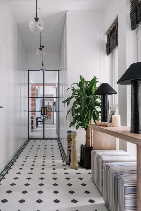 A Mumbai apartment entrance passage with white wall panelling, patterned flooring, a timber console and plants