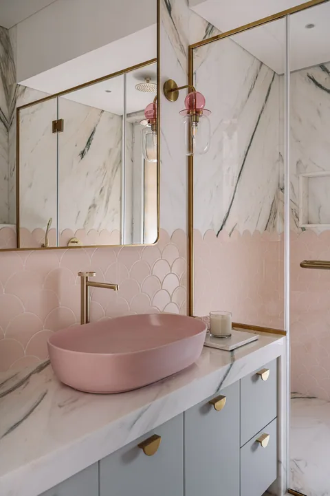 A Mumbai apartment bathroom with pink basin bowls, pale marble surfaces, a long fitted vanity and brass fittings