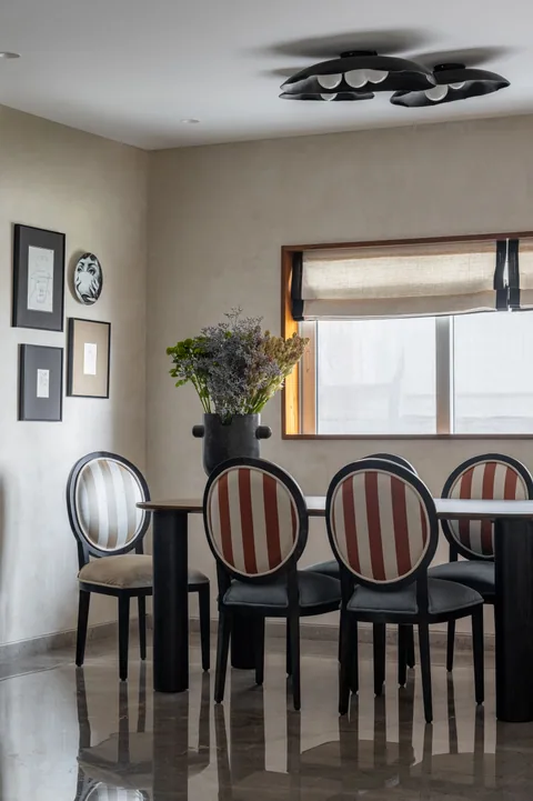 A Mumbai apartment dining space with a dark oval table, cane-back chairs, framed artwork and a window